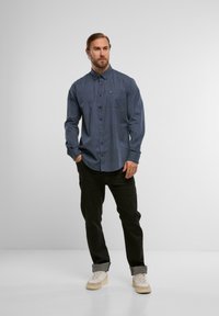 Navy-blaues Hemd mit weißen Punkten, langen Ärmeln und einer Brusttasche, kombiniert mit schwarzen Hosen und cremefarbigen Sneakers.