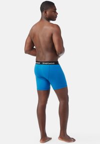Boxer da uomo blu realizzati in morbido tessuto, con una cintura nera a contrasto con il logo "Smartwool". Il modello è mostrato di spalle.
