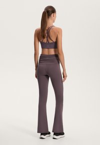 Lila sportos öltözet, amely crisscross hátú sportmelltartóból és illeszkedő, harangszárú leggingsből áll, az elasztikus anyagból készült, redőzött derékkal.