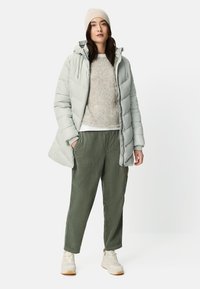 Light grey puffer jacket with a hood, textured knit beige sweater, olive green trousers, and beige sneakers with a white sole.