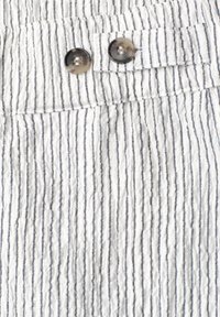 Tissu blanc avec de fines rayures noires verticales et deux boutons translucides foncés sur une taille froncée.