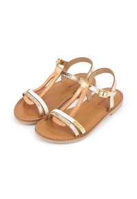 Sandalias con tiras que presentan cuero metálico dorado, dorado rosa y blanco, con suela plana y hebilla ajustable en el tobillo.