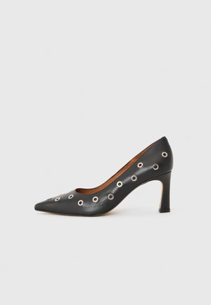 Black leather pump with a pointed toe, featuring metal grommets along the sides, and a mid-height stiletto heel. Smooth texture.