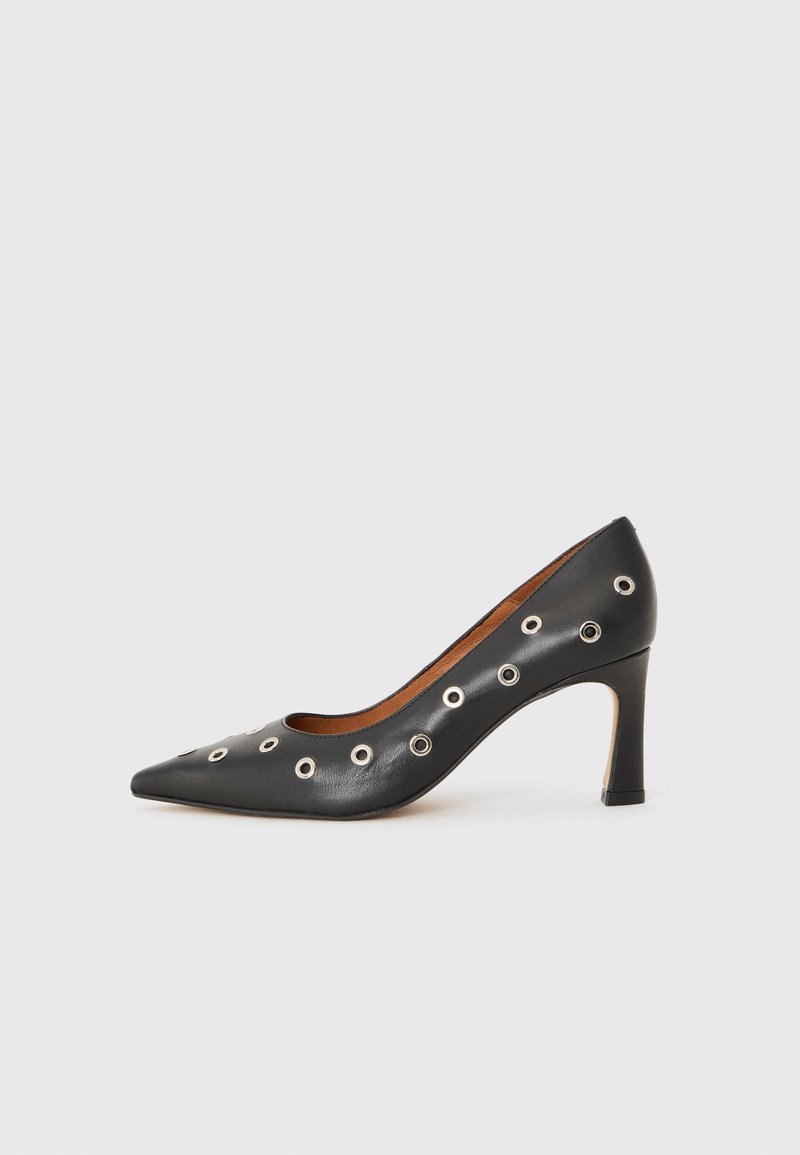 Sorte lærpumps med spiss tå, med metallringer langs sidene, og en midhøy stiletthels. Glatt tekstur.
