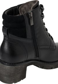 Bottine en cuir noir avec une finition texturée, doublure en fourrure, détail de fermeture éclair et un talon épais. Comprend plusieurs œillets pour les lacets.