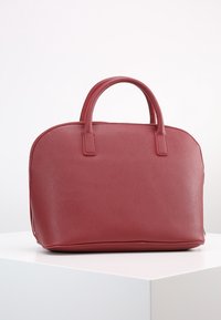 Červená texturovaná kabelka zaobleného tvaru s dvojitými vrchními uchy a zipovým uzávěrem. Hladký povrch a minimální akcenty z kovových částí.