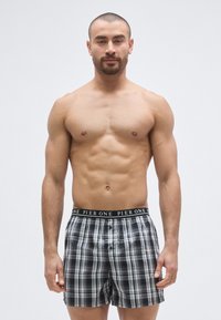 Boxer à carreaux noir et blanc avec ouverture à boutons et ceinture noire arborant le logo « PIER ONE ». Tissu lisse, coupe ample.