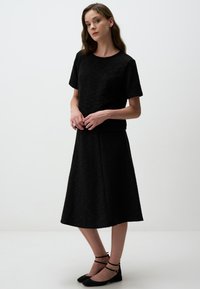 Zwart twee-delig outfit met een top met korte mouwen en een rok tot de knie, vervaardigd uit textuurstof met een subtiel patroon en afwerkingen.