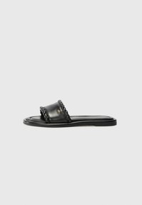 Black leather sandal with a woven strap detail, flat sole, and a sleek design. Smooth texture and minimalistic profile.