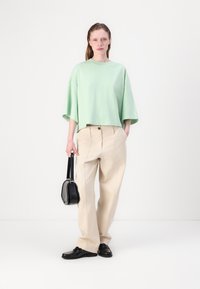 Majica mint zelene boje s kratkim rukavima, široke kreme hlače, crna torba za ruke i crne cipele s teksturiranim detaljima. Minimalistički dizajn.