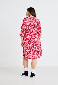 Κόκκινο φόρεμα με λευκό σχέδιο φύλλων, τρία τέταρτα μανίκια και ζώνη στη μέση. Φοριέται με μαύρα sneakers και λευκές κάλτσες.