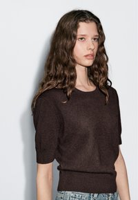 Bruin, kortekorte gebreide trui met een ronde hals, een aansluitende taille en een zachte textuur, gecombineerd met lichtblauwe spijkerbroek.