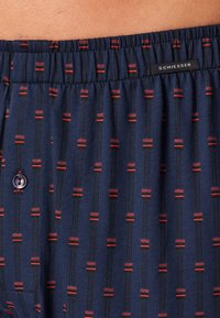 Mørkeblå boxershorts med et gentaget mønster af røde og sorte striber. Elastisk talje med et lille SCHIESSER-etiket og en knapdetalje.