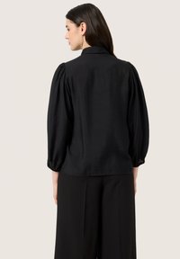 Blusa negra con una textura lisa, con cuello camisero y mangas abullonadas, puños fruncidos y un corte relajado.