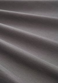 Pelēks audums ar gludu tekstūru, kas satur smalkus krokus. Materiāls šķiet viegls ar smalku austumu un vienotu krāsu.