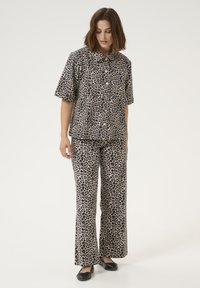 Outfit od dva dijela s uzorkom leopard kože, koji se sastoji od košulje s kratkim rukavima na dugmad i flared hlača u bež i crnoj boji, izrađen od mekanog materijala.