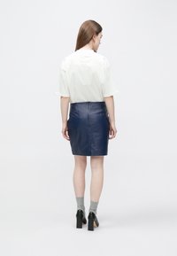 Bela srajca s kratkimi rokavi, mornarsko modra usnjena krilo do sredine stegna, gladke teksture, kombinirano s črnimi čevlji z blok peto in sivimi nogavicami.