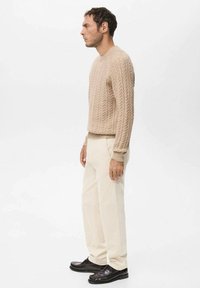 Beżowy sweter z dzianiny warkoczowej z okrągłym dekoltem, zestawiony z jasnobeżowymi sztruksowymi spodniami i czarnymi skórzanymi butami. Prosty fason i fakturowana dzianina.