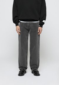 Jeans anchos de color gris oscuro con una textura suave y detalles de costura, combinados con un sudadera negra y zapatos negros brillantes.