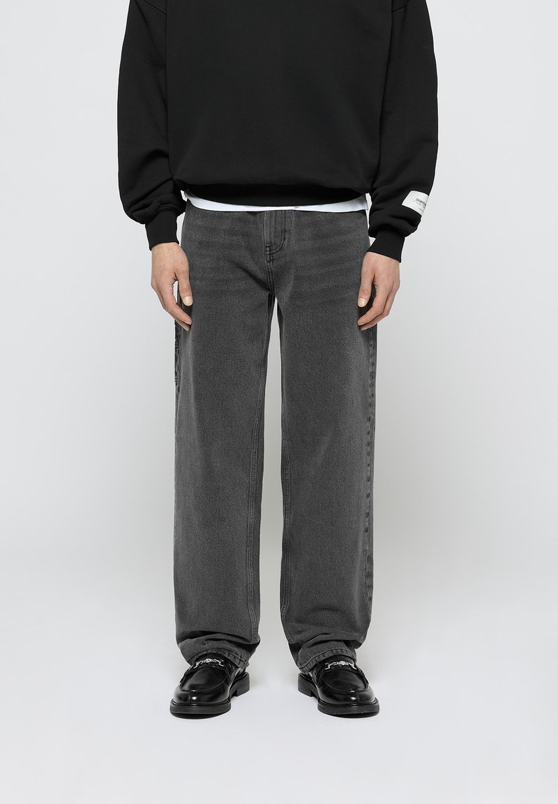 Jeans anchos de color gris oscuro con una textura suave y detalles de costura, combinados con un sudadera negra y zapatos negros brillantes.