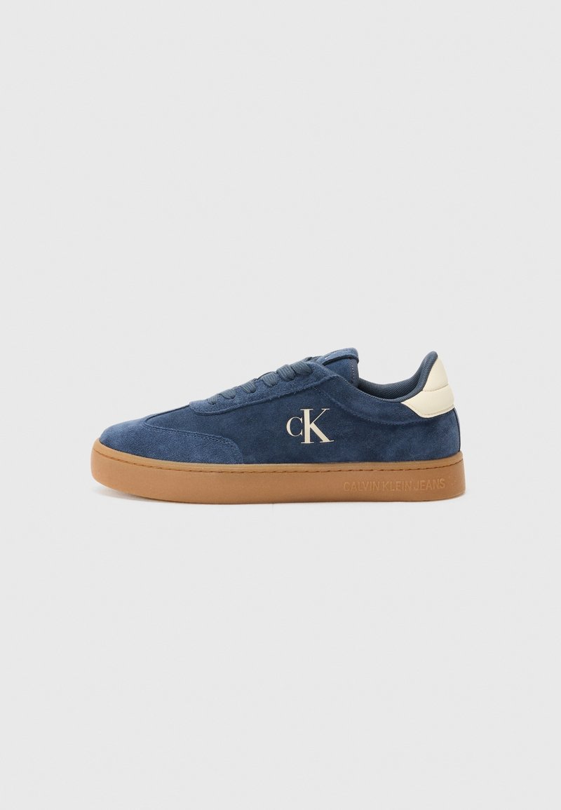 Baskets basses en daim bleu avec semelle en caoutchouc marron clair, languette blanche au talon et logo "cK" sur le côté.