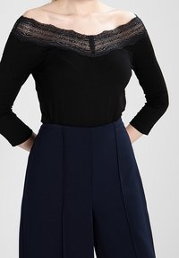 Svart off-shoulder topp med spetsdetalj vid halsringningen, kombinerad med högmidjade marinblå byxor med skräddarsydd, vida ben.