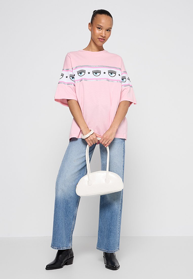 T-shirt surdimensionné rose avec des motifs d'yeux et d'étoiles, accents bleu clair ; associé à un jean en denim léger taille haute et un sac à main blanc.