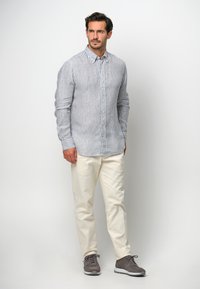 Camicia a righe azzurro chiaro e bianca, tessuto leggero, maniche lunghe, abbinata a pantaloni crema e scarpe da ginnastica grigie.