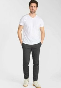 Witte V-hals T-shirt gecombineerd met donkergrijze slim-fit broek. Het model draagt lichte sneakers, die een minimalistisch ontwerp en casual stijl uitstralen.