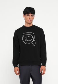 Felpa nera in cotone con una grafica disegnata a linea bianca di un viso con occhiali da sole. Collo a giro classico e polsini a costine.
