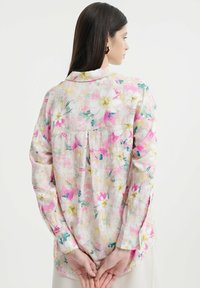 Blumiges Herrenhemd aus leichtem Stoff mit pinken, gelben und grünen Mustern. Lange Ärmel, ein Kragen und eine Faltenoptik im Rückenbereich.