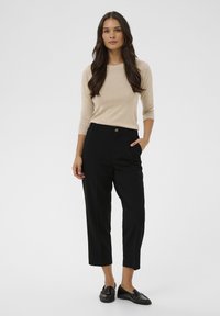 Pull beige à manches longues ; pantalon noir taille haute avec bouton ; texture lisse ; mocassins plats noirs ; fond neutre.