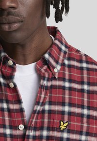 Camicia a maniche lunghe a quadri rossi e blu navy con dettagli bianchi. Presenta un piccolo logo ricamato giallo sul petto e un design classico del colletto.