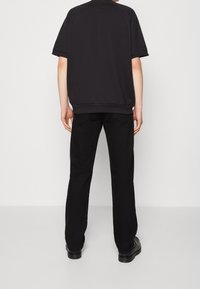 Svart oversized t-shirt med korta ärmar och rundad nederkant, parat med svarta raka byxor; tyget verkar jämnt och enhetligt i färgen.