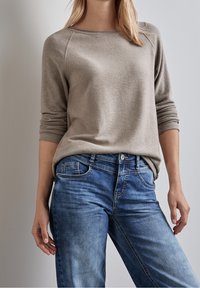 Beżowy sweter dziergany z szerokim dekoltem i długimi rękawami, w połączeniu z jasnoniebieskimi dżinsami o klasycznym fasonie z pięcioma kieszeniami.