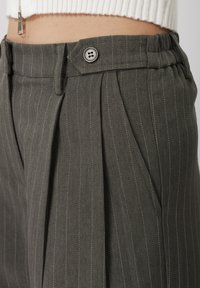 Σκούρα γκρι παντελόνια με ρίγες, κατασκευασμένα από υφασμάτινη υφή, με εμπρόσθια πιέτα, κλείσιμο με κουμπί και διακριτικές λευκές ραφές ως διακοσμητικά στοιχεία.