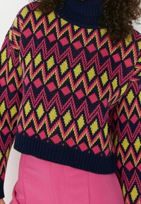 Sweter wykonany na szydełku z granatową bazą i żywym, zygzakowatym wzorem w różowym i żó�łtym kolorze, o krótkiej długości, z prążkowanym golfem.
