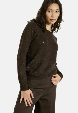 Maglione a maglia marrone con scollo a giro e maniche lunghe, arricchito da pagliuzze metalliche per un tocco di texture. Abbinato a pantaloni scuri.