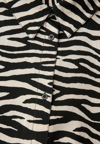 Chemise à rayures zebra noir et blanc avec un col, boutonnage sur le devant et un tissu léger à finition texturée.