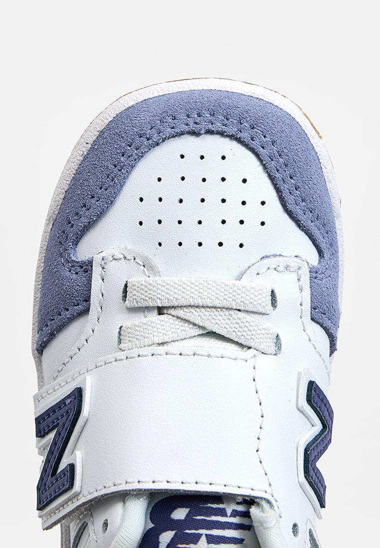 Sneaker bianco con accenti in suede azzurro chiaro e dettagli blu navy. Presenta una punta perforata, lacci e una fascia regolabile. Suola in gomma.