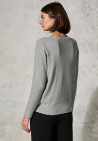Grau gerippter Strickpullover mit langen Ärmeln, weitem Ausschnitt und lockerer Passform, kombiniert mit schwarzen Hosen. Glatte Textur und lässiges Design.