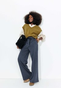 Un gilet surdimensionné vert texturé sur une chemise blanche rayée, associé à un pantalon à carreaux bleu amples et des chaussures imprimé léopard. Sac noir inclus.