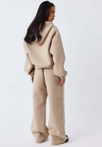 Sudadera beige oversize con capucha y pantalones anchos a juego. Textura suave y ajuste relajado con detalles de costuras visibles.