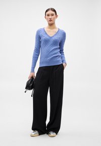 Gaiši zils adīts džemperis ar V veida kaklu, kombinēts ar melnām platām bikšu kājām. Izcelts ar mazu melnu somiņu un sudraba krāsas apaviem.