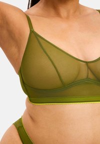 Vihreä läpikuultava bralette, jossa on kolmiomainen muotoilu, ja siinä on vastakkaista neonvihreää reunustusta sekä säädettävät hihnat. Sujuva pinta ja minimalistinen muotoilu.
