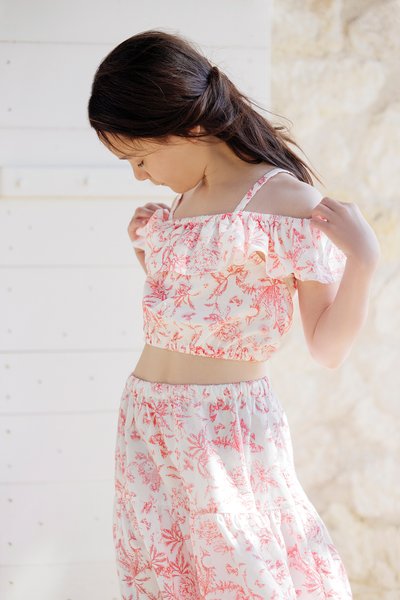 Top cropped floral com mangas em babados em tecido leve, apresentando padrões em rosa e branco. Combinado com uma saia floral correspondente.