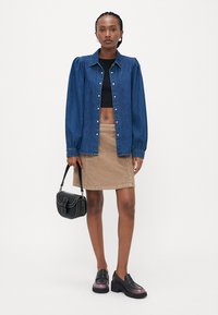 Jeans-skjorte med puffermer, svart crop top, beige kordfløyelskjørt og svarte platåsko. Svart crossover-veske med detaljer.