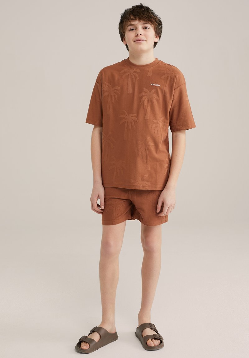 Brun bomull kortärmad t-shirt och shorts-set med palmträdsmönster, parat med bruna slidesandaler. Enkel, avslappnad passform.