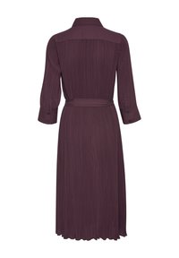 Lila pitkähihaine mekko, jossa on kauluksellinen pääntie, pleated-tekstuuri ja vyötärölle kiristettävä vyö. Helma on hieman levenevä ja ulottuu säärelle.