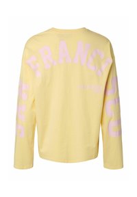 Żółta koszula z długim rękawem z różowymi blokowymi literami tworzącymi napis „FRANCI” na plecach oraz „CALIFORNIA 1987” po prawej dolnej stronie.